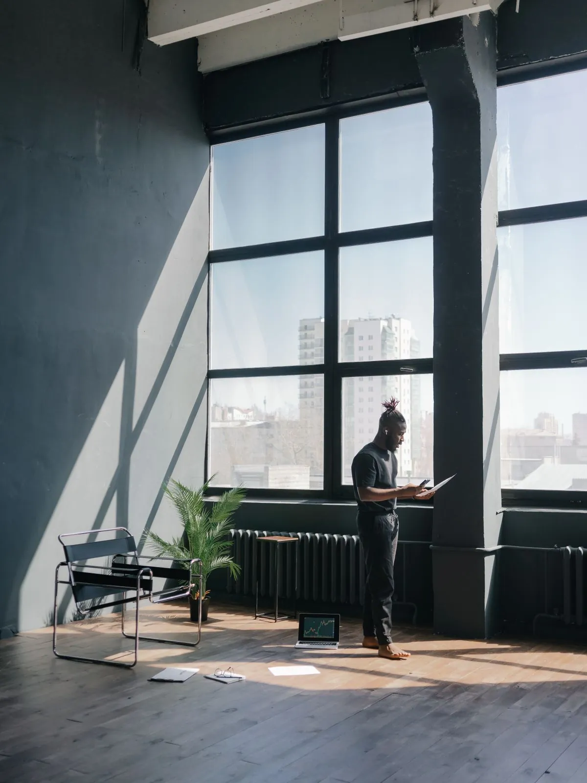 A founder reading on a laptop by the tall windows of a loft office